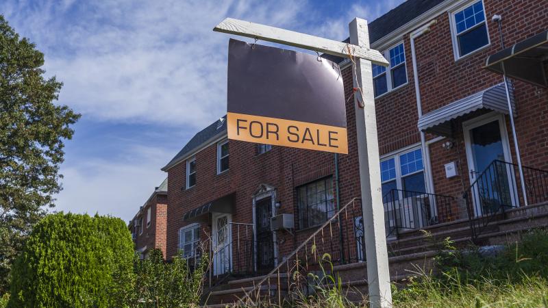 Picture of "for sale" sign in front of brick building with overgrown grass